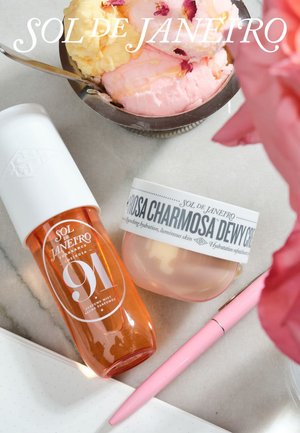Brume parfumée Sol de Janeiro, crème hydratante, stylo rose, carnet ouvert et bol de glace pêche et rose avec des pétales de fleur sur une surface en marbre.
