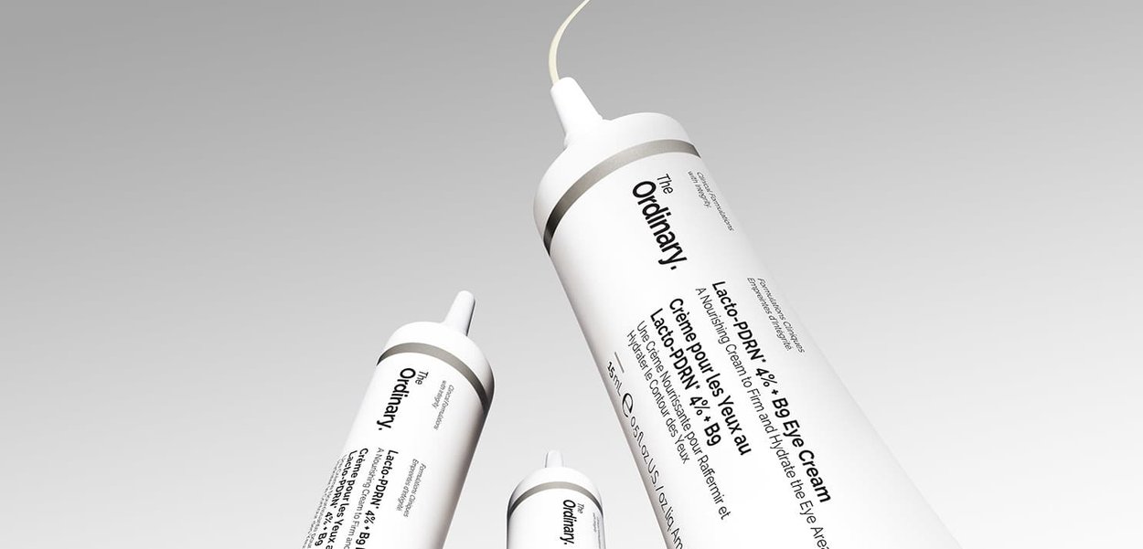Tres tubos de The Ordinary Lacto-PDRN 4% B9 Crema de Ojos sobre un fondo liso gris claro, mostrando las etiquetas del producto y tapas blancas.