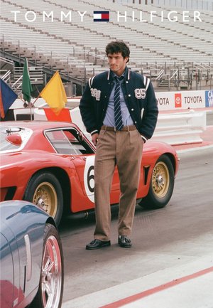 Tommy Hilfiger varsity jacket in navy with white accents, light blue shirt, beige trousers, and black shoes, standing near a vintage red car.