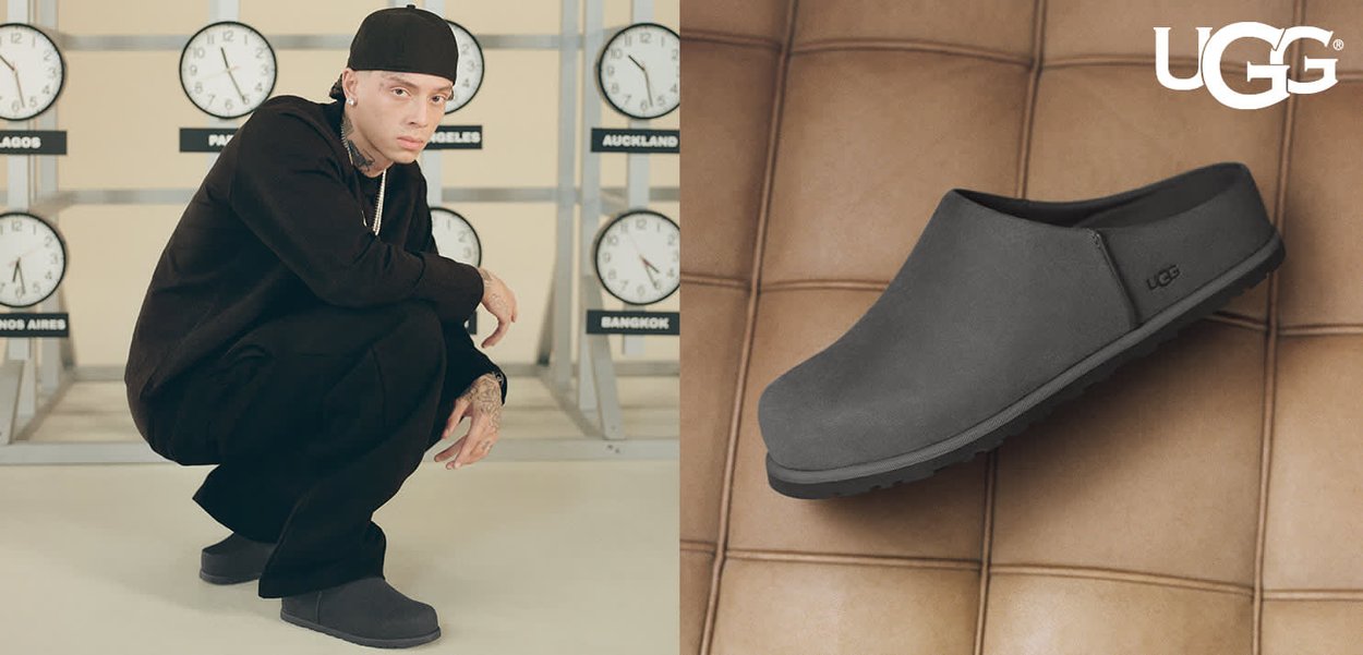 Un homme habillé de noir portant des chaussures UGG noires sans lacets s'accroupit à côté d'horloges affichant les heures mondiales ; gros plan sur la chaussure posée sur une surface en cuir.