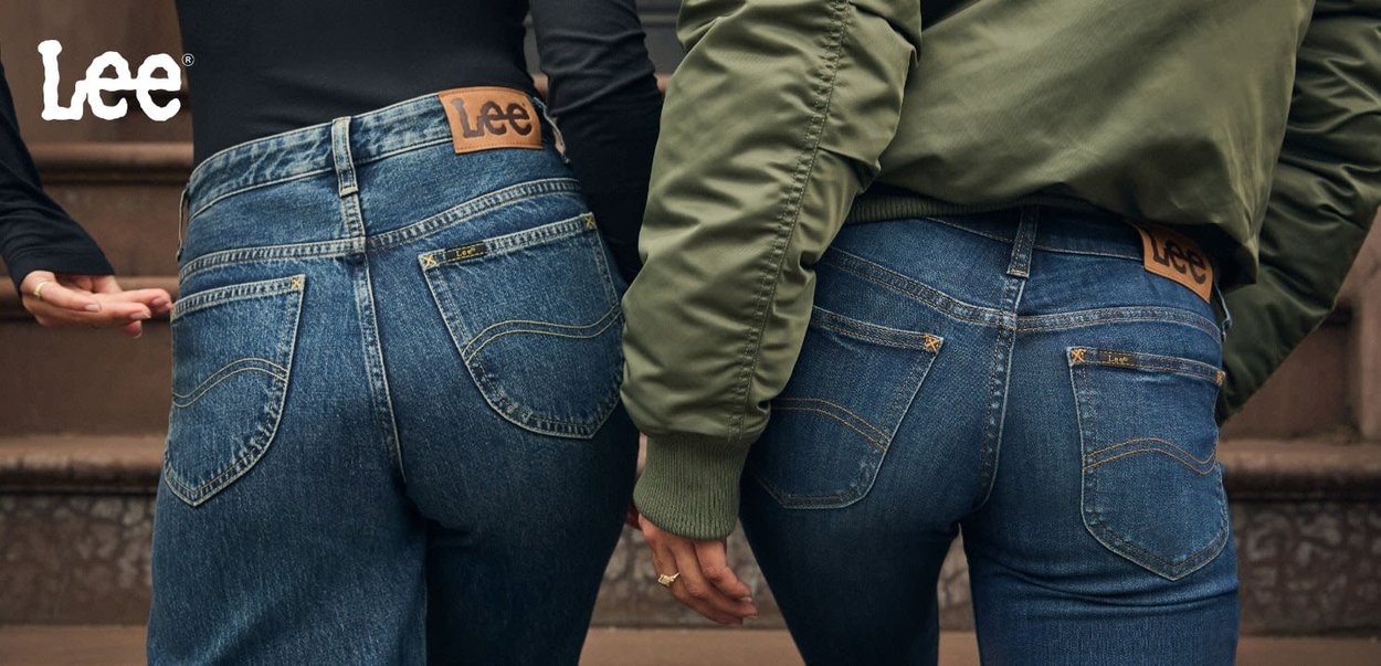 To par med blå denimjeans med karakteristiske lommer, gullsting og lærlogoer. En person har på seg en svart topp, den andre en olivengrønn jakke.
