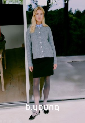 Cardigan grigio a maglia con bottoni in perle, indossato sopra una camicia a righe blu, abbinato a una gonna nera e collant trasparenti, completato da scarpe nere.