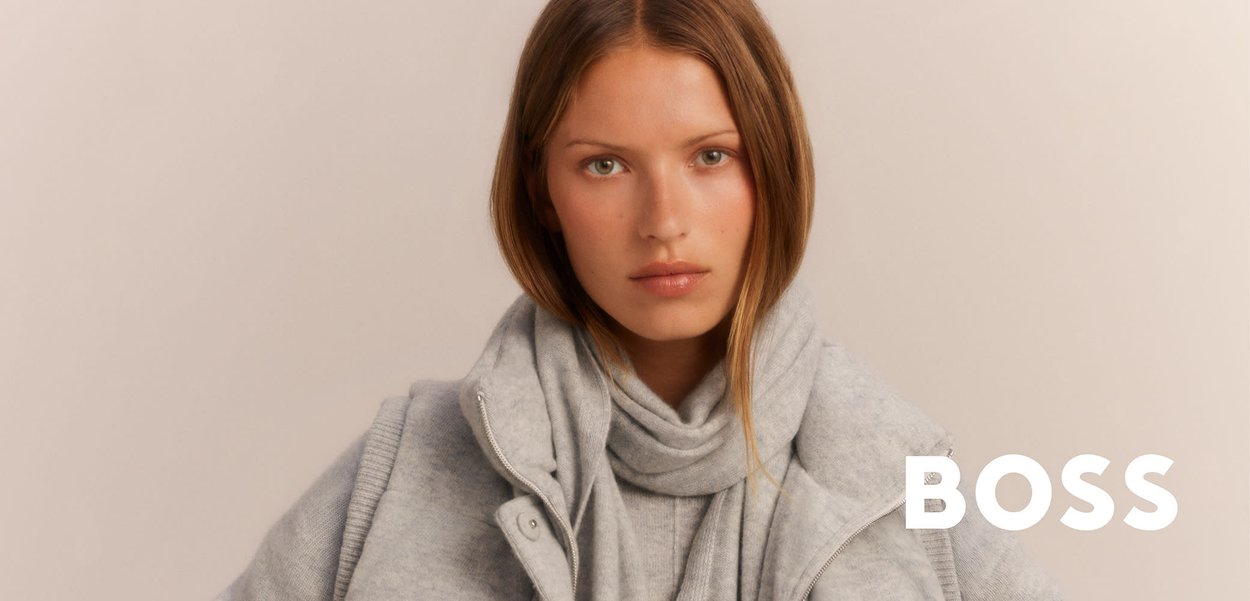 Grauer gestrickter Pullover und Schal, die unter einer Reißverschlussjacke getragen werden; weiche Textur und neutrales Farbschema. Branding an der rechten Seite.