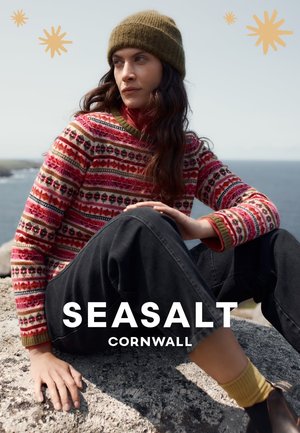 Strikket sweater med rødt, pink og grønt mønster; rund hals og lange ærmer. Båret med løse sorte bukser og en grøn strikket hue.