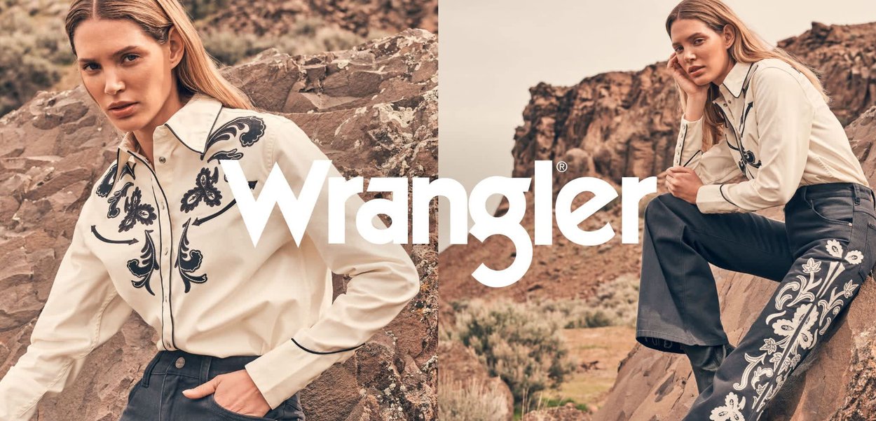 Biała koszula na guziki z czarnym obszyciem, ciemne spodnie z wysokim stanem ozdobione białą florystyczną haftowaną aplikacją, na tle skalistego krajobrazu.