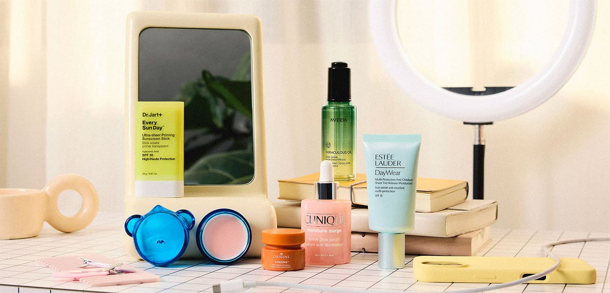 Produits de soins de la peau disposés sur une table avec un miroir, des livres, une lampe anneau et une coque de smartphone jaune dans une pièce bien éclairée.