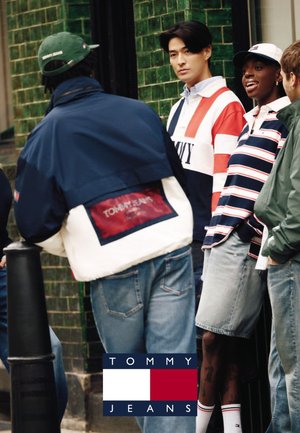Quatre jeunes adultes vêtus de vêtements décontractés Tommy Jeans se tiennent et discutent en plein air près d'un mur carrelé vert.