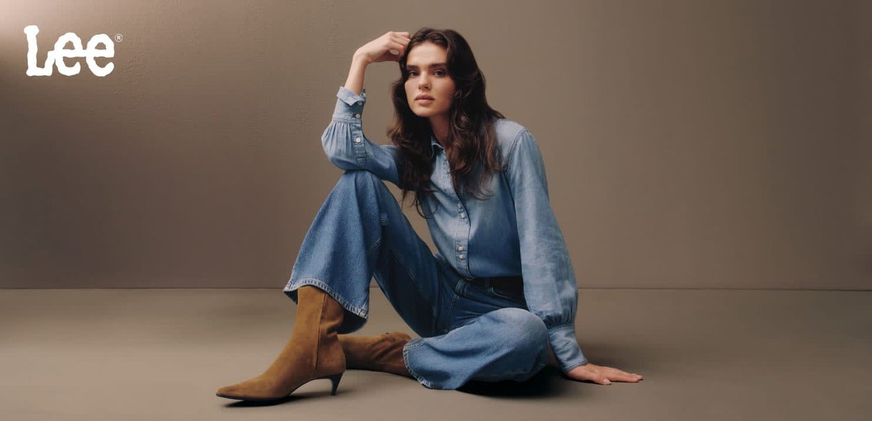 Chemise en denim et jeans larges en bleu clair, assortis à des bottines en daim beige à la cheville. Fond neutre avec le logo "Lee" en haut à gauche.