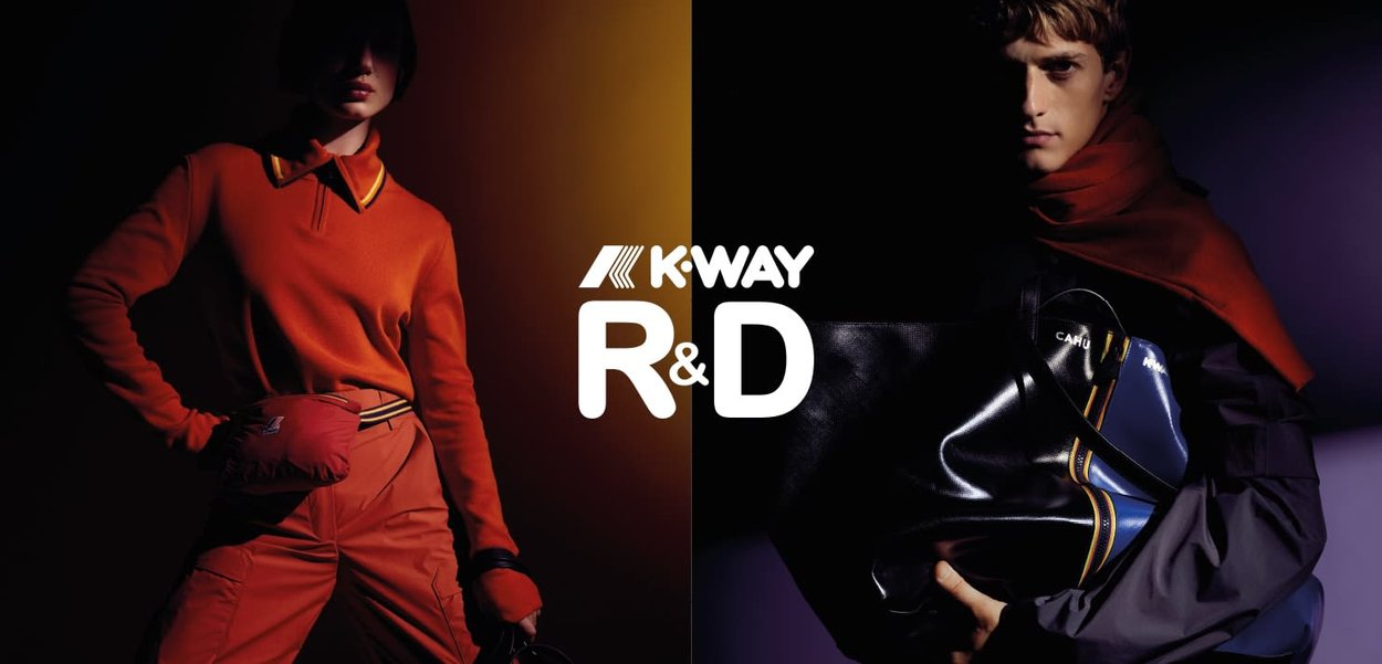 La ropa K-Way R&D presenta un polo de manga larga de color naranja brillante y pantalones a juego. El modelo masculino sostiene un bolso negro y azul con acentos amarillos.