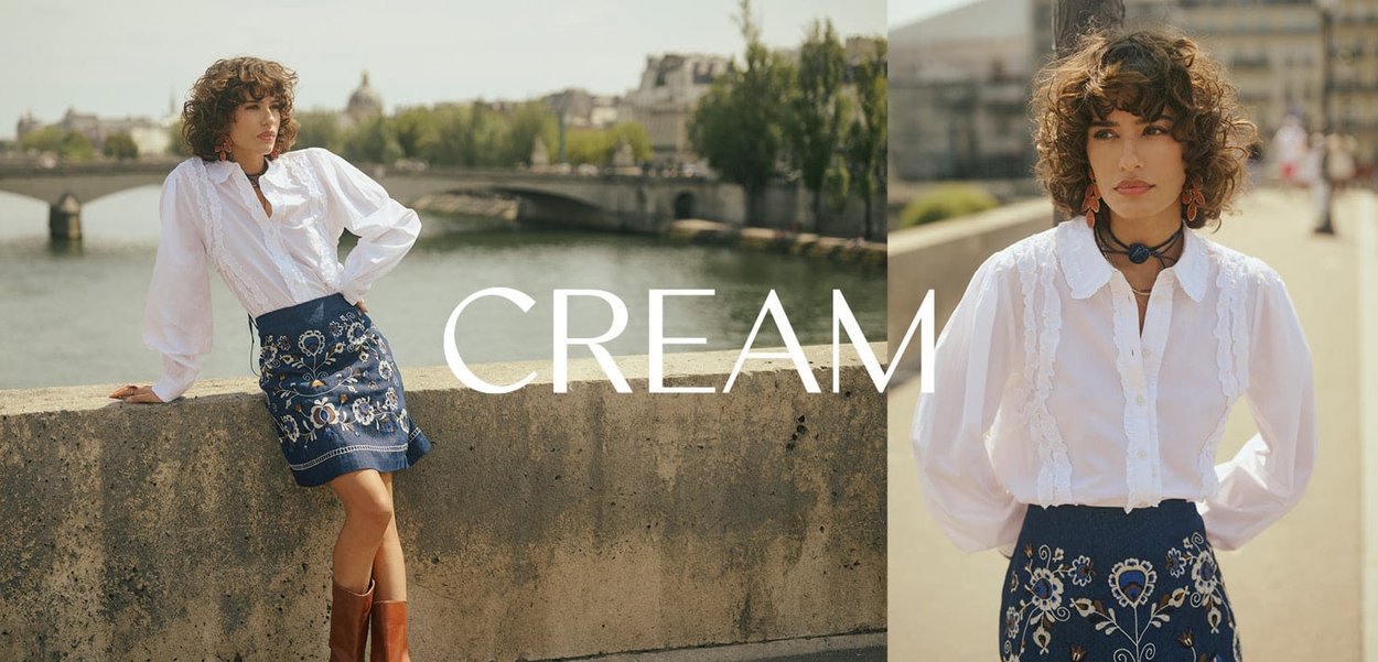 White blouse with ruffled details and a collar, paired with a blue embroidered skirt featuring floral patterns, worn with brown knee-high boots.