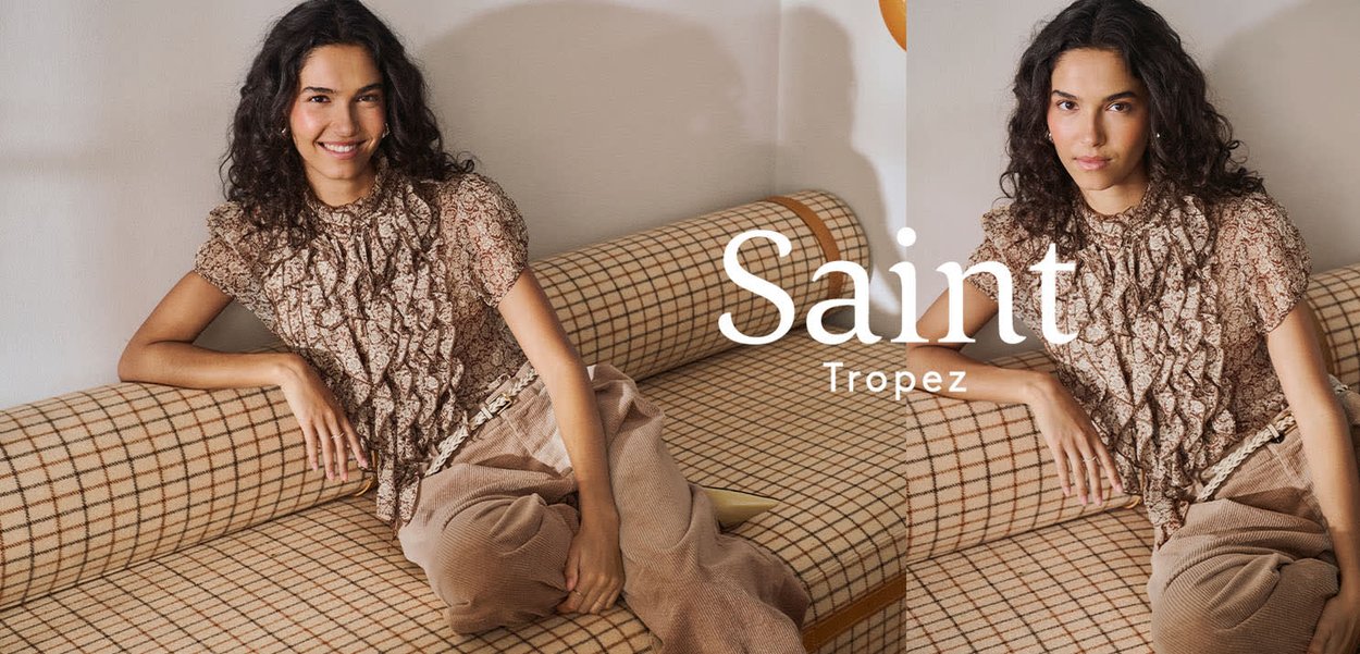 Kvinde med krøllet hår iført en mønstret bluse og beige bukser, der læner sig tilbage på en ternet sofa med teksten Saint Tropez.