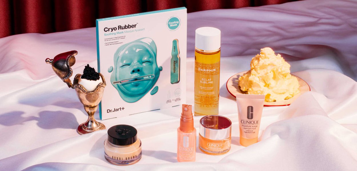 Dr. Jart+ Cryo Rubber mask kit in a turquoise box, surrounded by skincare products in various containers and textures on a white satin surface.