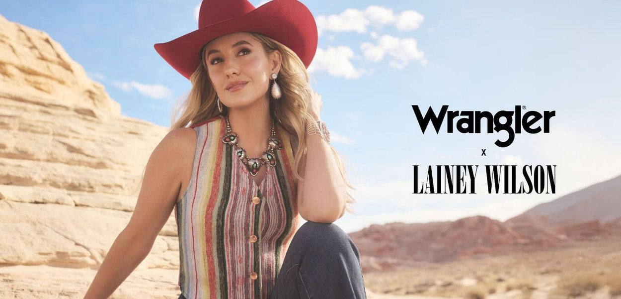 Top a maniche corte a strisce verticali multicolori con bottoni. Abbinato a jeans scuri e un cappello da cowboy rosso. Brand Wrangler x Lainey Wilson.