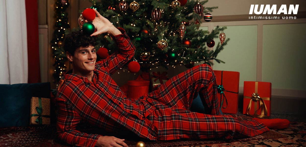 Set di pigiami a quadri rossi con maglia con bottoni e pantaloni larghi. La modella posa accanto a un albero di Natale decorato e regali colorati.