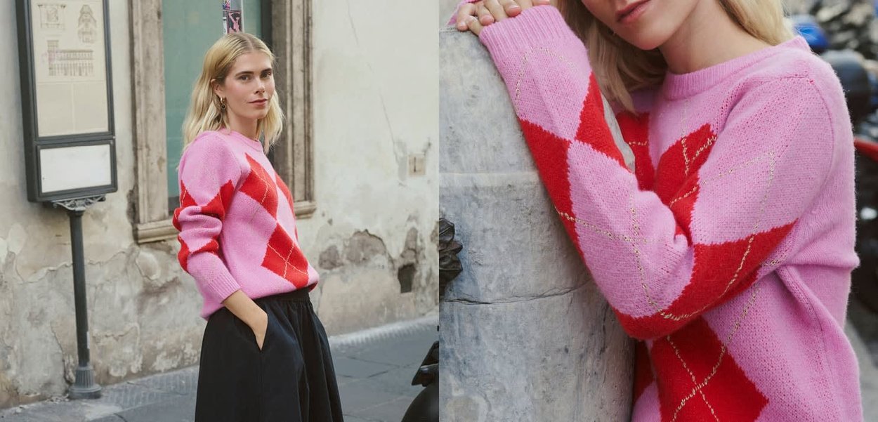 Rosa und rot kariertes Pullover mit weichem Strickmaterial. Lange Ärmel und gerippte Bündchen. Modell posiert vor einer Steinmauer.