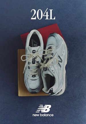 Scarpe da ginnastica bianche con pannelli in rete e materiale sintetico, caratterizzate da accenti grigi e logo, appoggiate su due scatole di colori differenti.