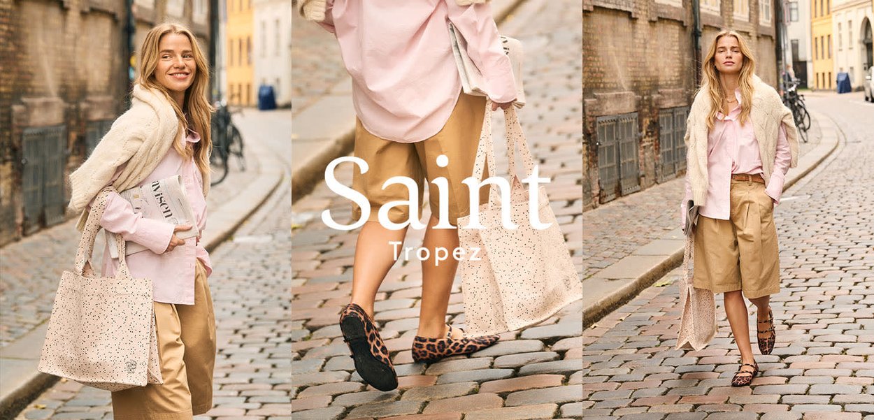 Frau geht auf Kopfsteinpflasterstraße, trägt beige Shorts, pinkes Shirt, cremefarbenen Strickpullover, Leoparden-Ballerinas und trägt eine perforierte Tragetasche.