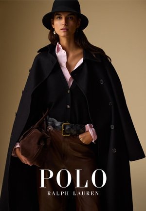 Manteau noir avec de gros boutons, superposé sur un gilet noir et une chemise rose. Un pantalon en cuir marron et un sac à main complètent le look. Chapeau noir et boucles d'oreilles en or.