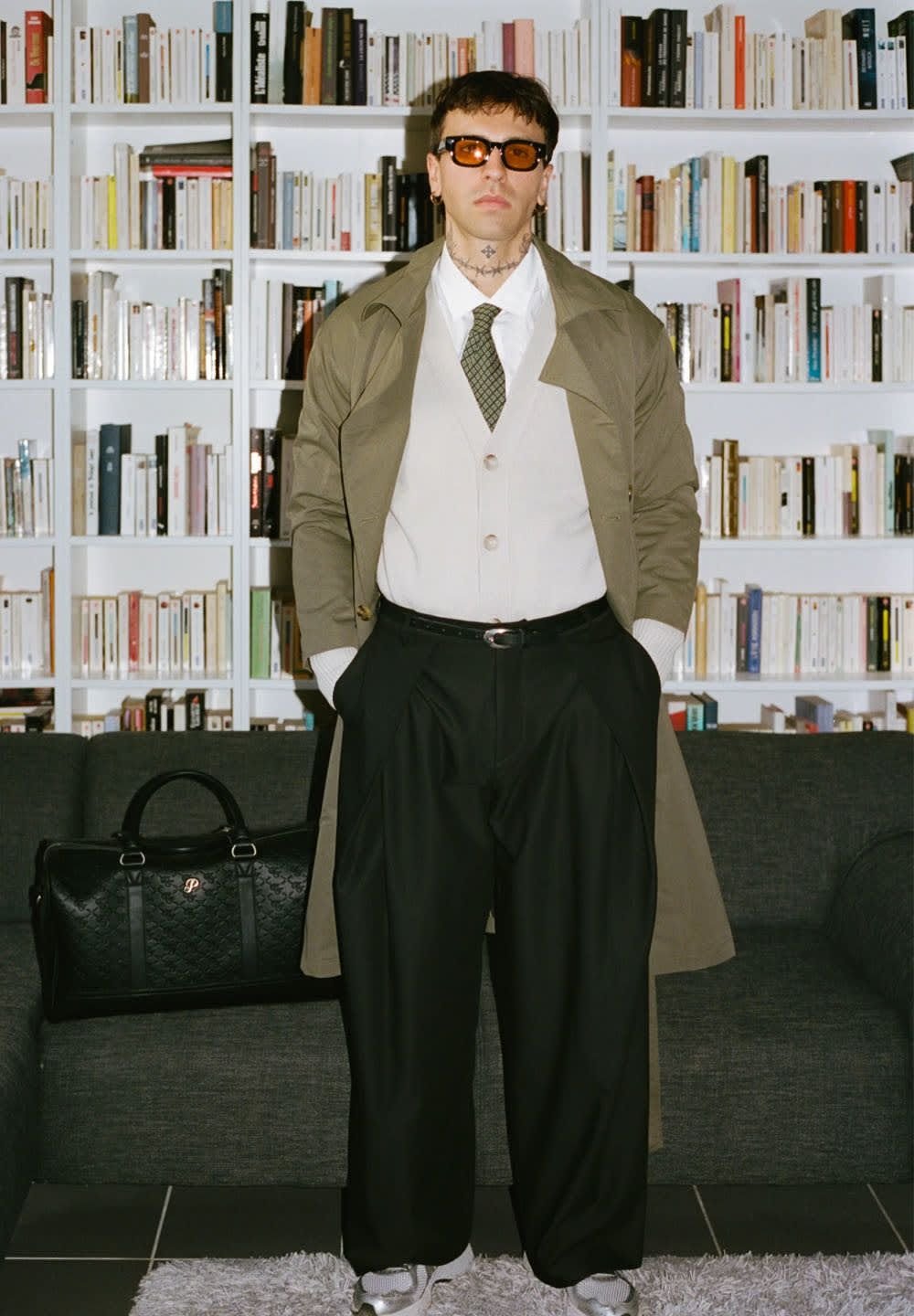 Must have mustreeritud kott, khakivärvi trench coat, valge kardigan, roheline lips, ülemõõdulised mustad püksid ja hallid tossud raamatuhiiu taustal.