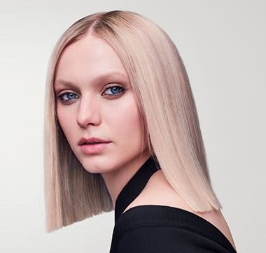 Straight, shoulder-length blond hair with a smooth texture. Model features blue eyes and a clean, minimalistic black outfit with an asymmetrical neckline.