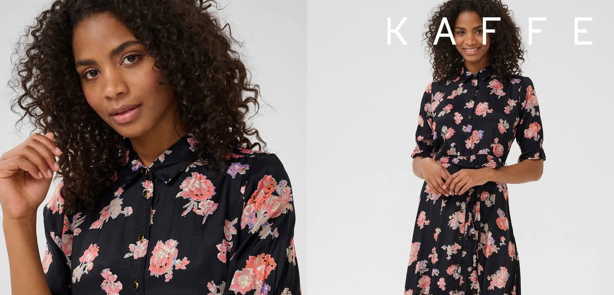 Sort blomsterkjole med korte ærmer, prydet med store lyserøde og lilla blomster, krave og knaplukning. Glat stoftekstur.