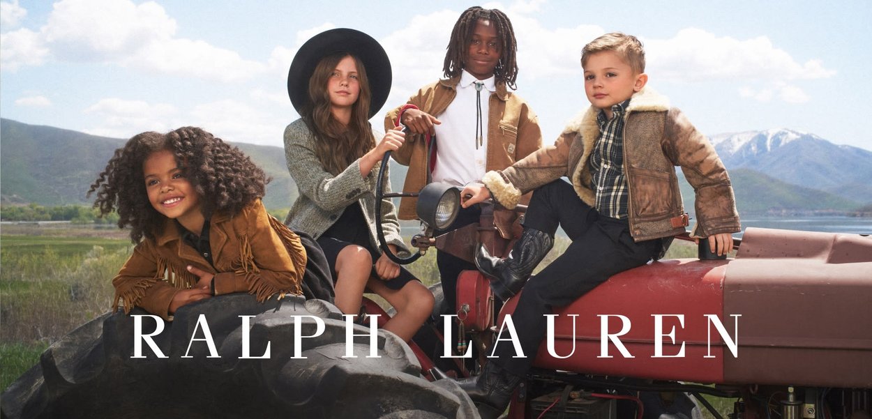 Neljä lasta poseeraa traktorilla. Heillä on päällään tekstuurillisia vaatteita ruskeassa ja vaaleanruskeassa, sekä musta hattu; yhdellä heistä on kiharat hiukset, mikä eroaa muista.