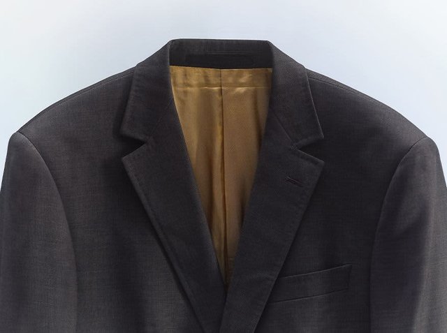 Dark gray blazer with a textured fabric, peaked lapel, single chest pocket, and golden lining visible at the collar and inside.