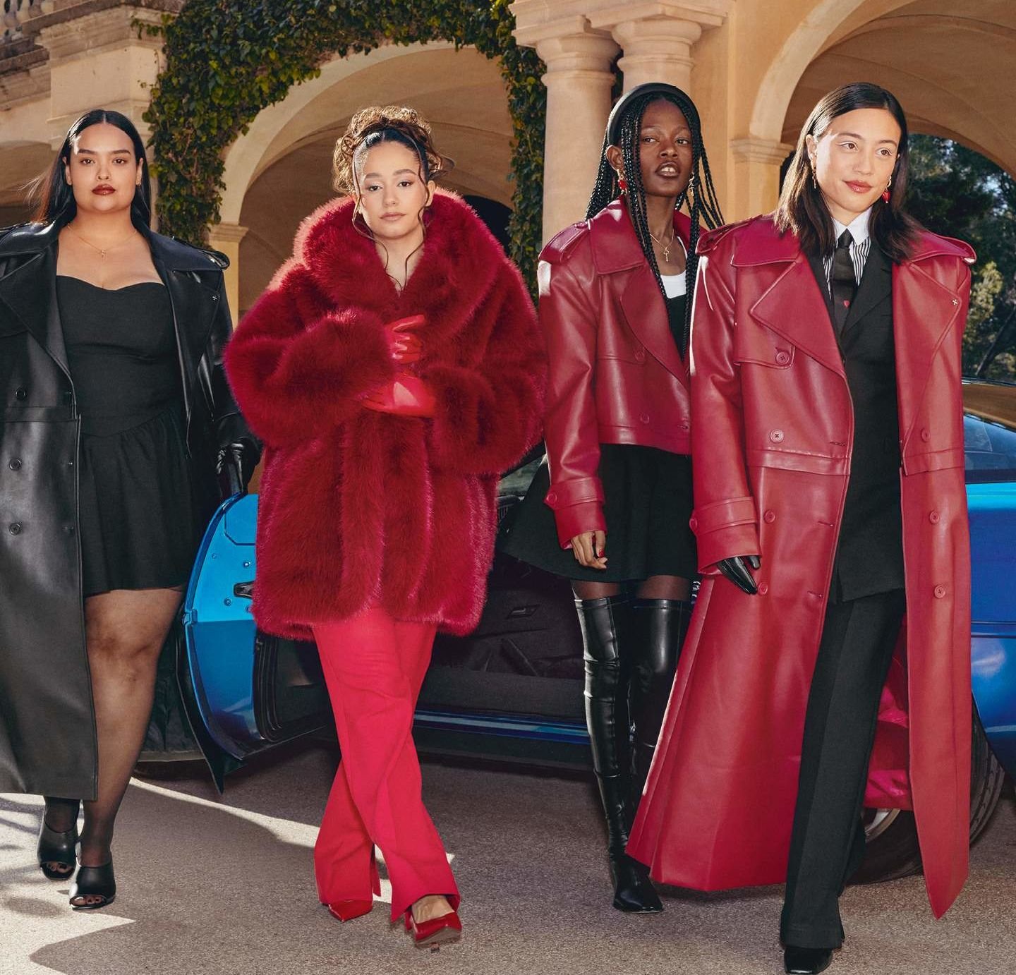 Quatre femmes se tiennent près d'une voiture bleue. Elles portent différentes manteaux, dont un manteau en fourrure rouge et une veste en cuir rouge, ainsi que des tenues et accessoires noirs.