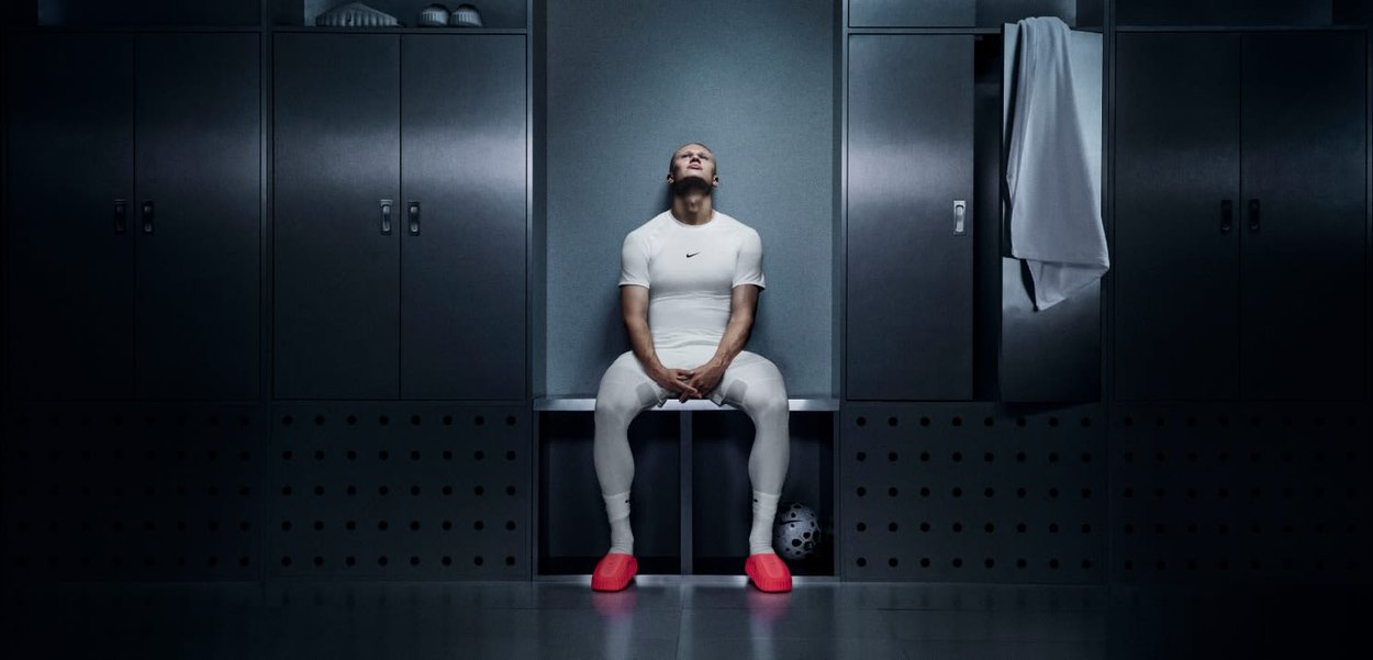 Wit Nike sporttopje en strakke broek gedragen door een zittend persoon in een kleedkamer, met felrode schoenen en donkergrijze kluisjes op de achtergrond.