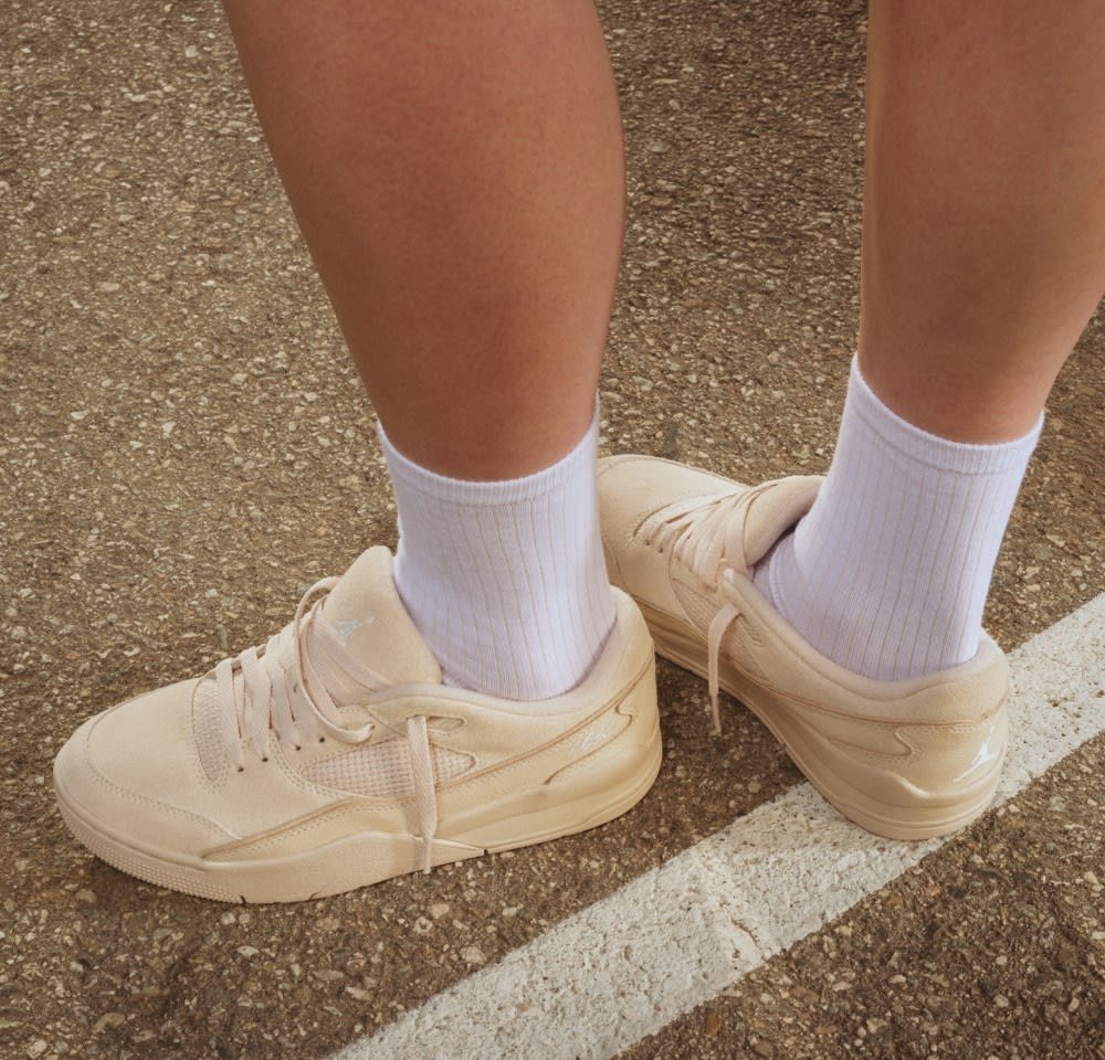 Baskets beige en daim, avec un panneau en maille, des lacets plats et une semelle en caoutchouc, portées avec des chaussettes blanches à côtes.