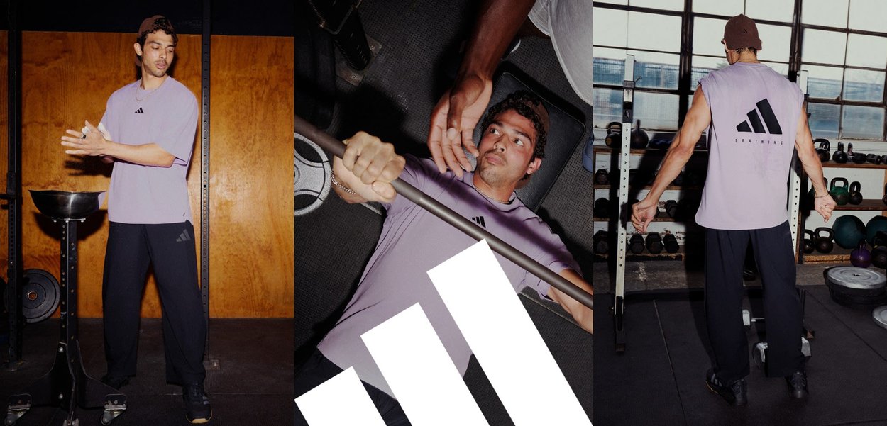 T-shirt d'entraînement sans manches de couleur lilas clair avec logo noir, associé à un pantalon noir. L'arrière-plan présente du matériel de gym et des poids.