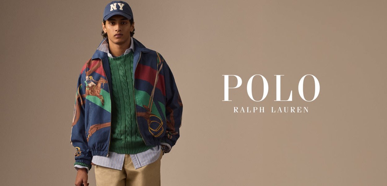 Veste coupe-vent marine et multicolore avec des graphismes équestres sur un pull en mailles vertes et une chemise col bleu, assortie à un pantalon beige.