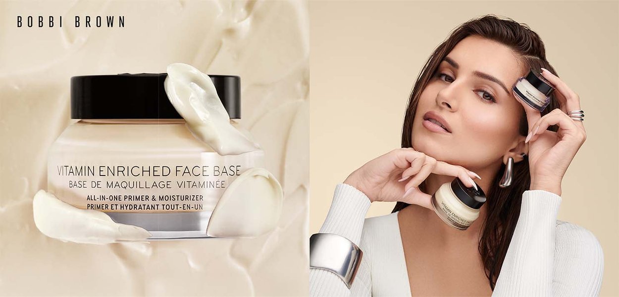 Bocal crème avec un couvercle noir étiqueté "Base de visage enrichie en vitamines", entouré d'une éclaboussure crémeuse. Personne tenant deux bocaux, portant un pull blanc.