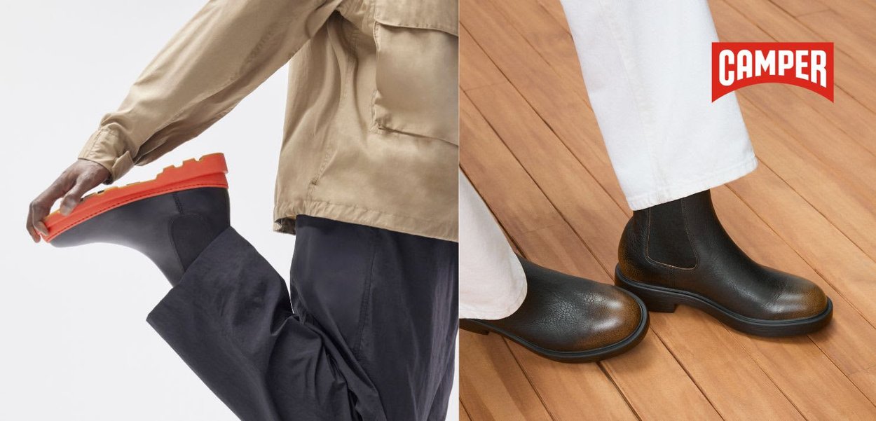 Schwarze Knöchelstiefel mit strukturierter Oberfläche und braunen Akzenten, kontrastierende orangefarbene Sohle, vor einem Holzboden-Hintergrund. Branding sichtbar.