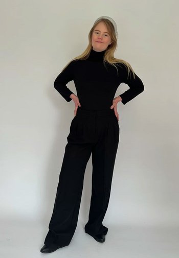 Svart polokrage och högmidjade svarta veckade byxor, med en avslappnad passform och mjuk yta, tillsammans med svarta skor.