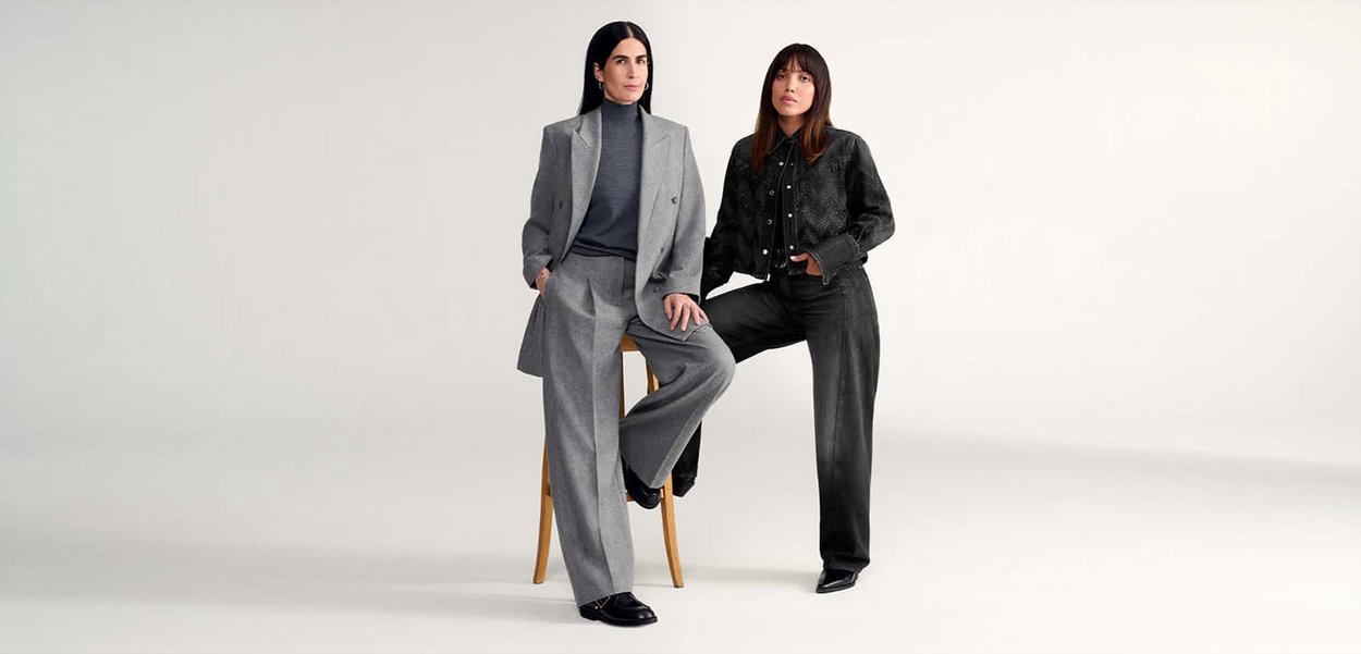 Blazer gris de doble botonadura y pantalones de pierna ancha usados por una persona, combinados con una chaqueta negra ajustada y jeans en otra. Texturas suaves evidentes.