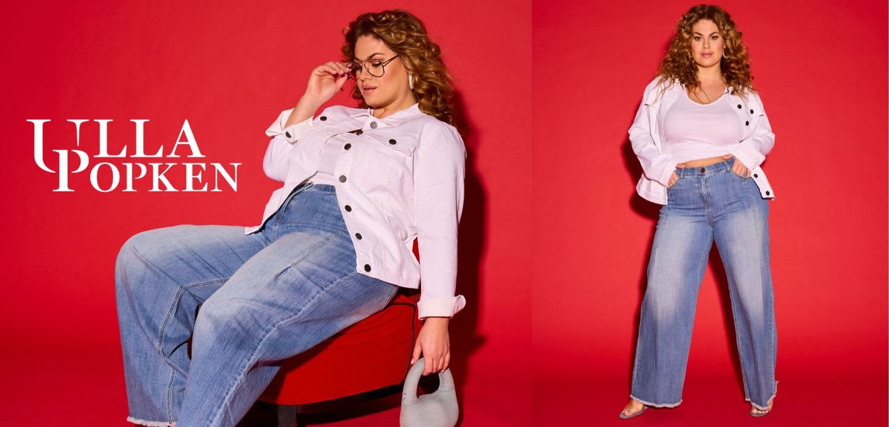 Witte spijkerjasje met zwarte knopen en opgerolde mouwen, gecombineerd met lichtblauwe jeans met wijde pijpen. Achtergrond is effen rood. Merkenlogo weergegeven.