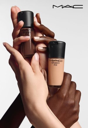 Hände mit unterschiedlichen Hauttönen halten zwei M·A·C Studio Fix Foundation-Flaschen vor einem weißen Hintergrund.