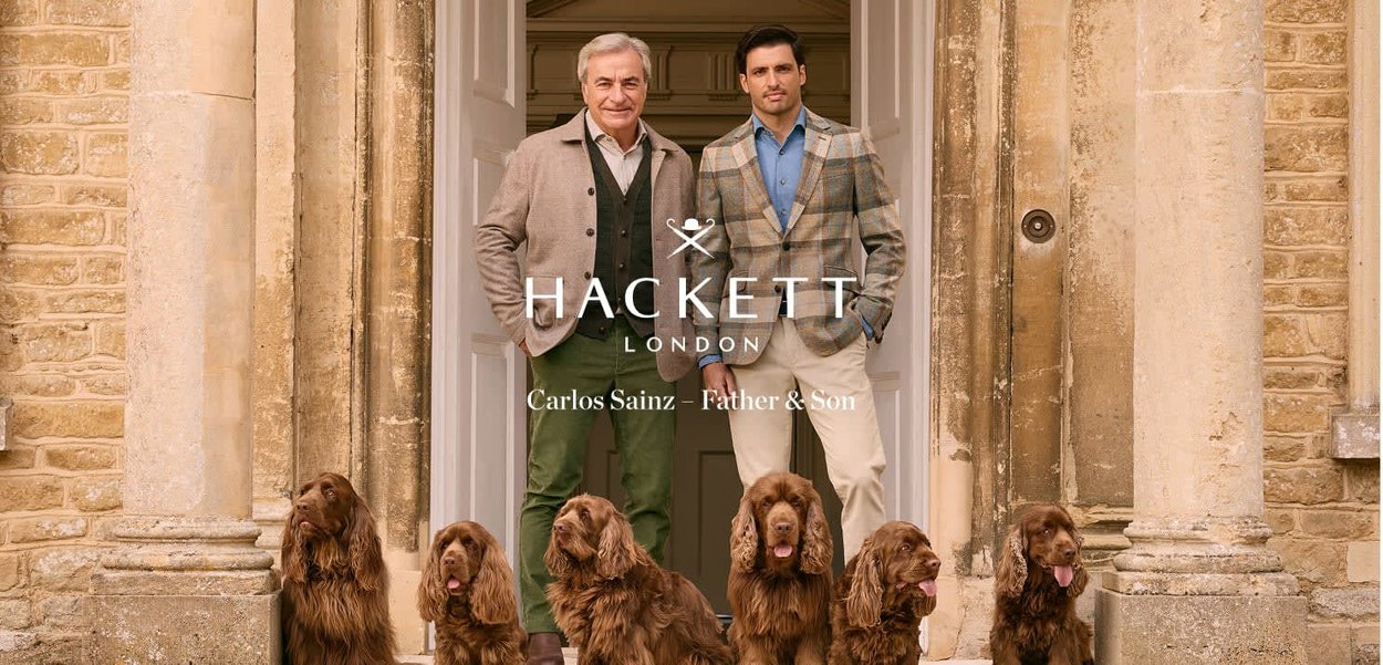 Twee mannen in op maat gemaakte outfits staan in een stenen deur, geflankeerd door vier bruine spaniels, met een klassieke stijl en een gedempte kleurenpalet.