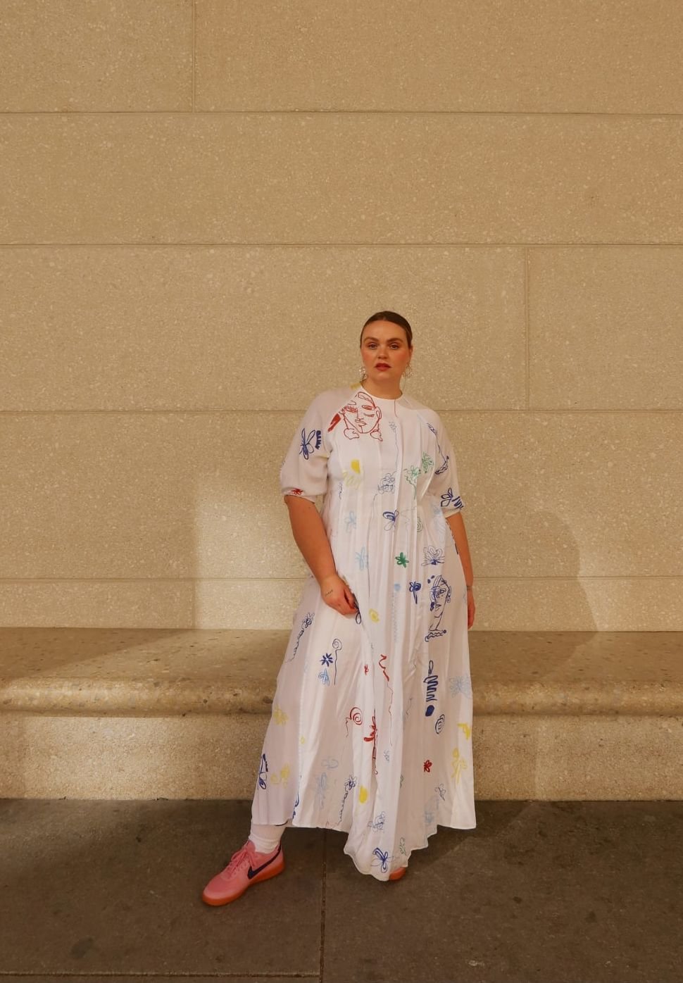 White dress with colorful doodles, short puff sleeves, knee-length, paired with pink sneakers. Simple design with a relaxed fit.