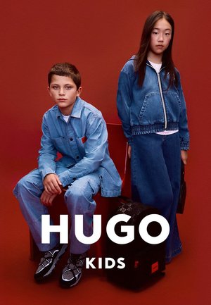 Denim-Outfits an zwei Kindern; eines in einer hellblauen Jacke und Hose, das andere in einer passenden Jacke und Maxirock. Schwarzer Rucksack auf dem Boden.