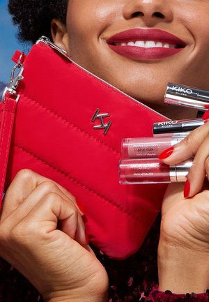 Red quilted pouch with silver zipper and logo. Holding three KIKO Milano lip glosses in clear and silver tubes. Bright red nails visible.