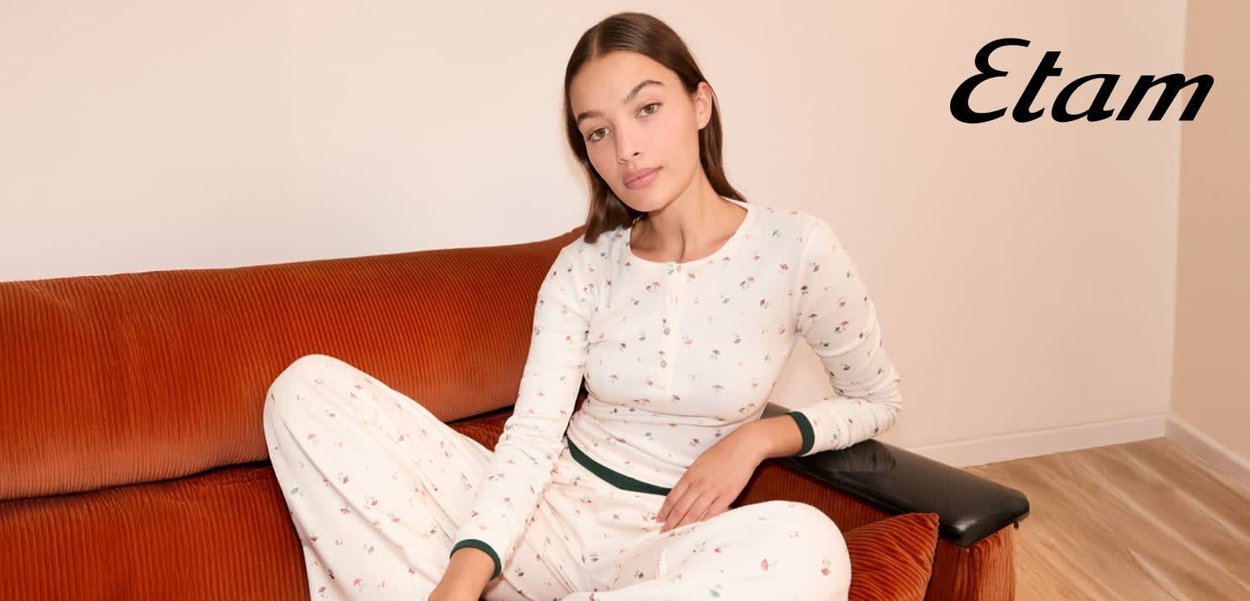 Biały zestaw do noszenia w domu z kwiatowymi wzorami, z długimi rękawami i zielonymi akcentami. Siedząca na teksturowanej, rdzawej sofie.