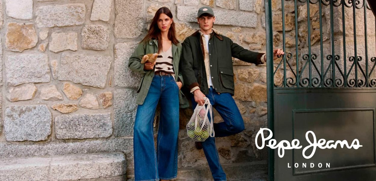 Zwei Personen posieren in lässigen Outfits. Die Frau trägt eine grüne Jacke und ein gestreiftes Oberteil, während der Mann eine dunkle Jacke mit Denim-Hosen anhat.