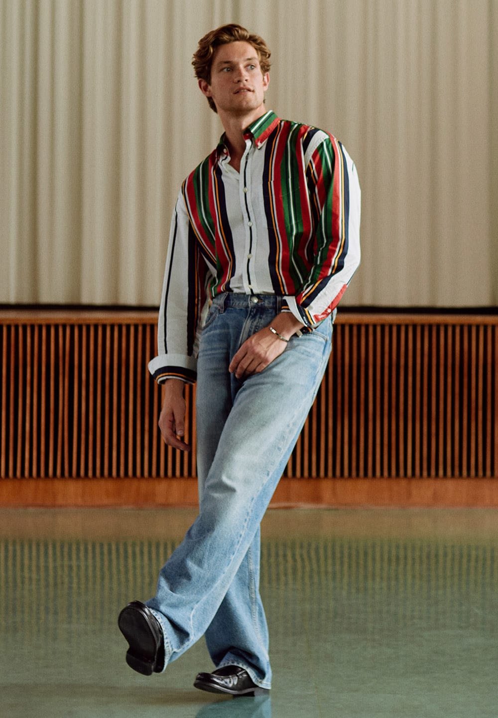 Multicolored striped shirt with red, green, and blue lines, paired with light blue denim jeans and black shoes, set on a smooth floor.