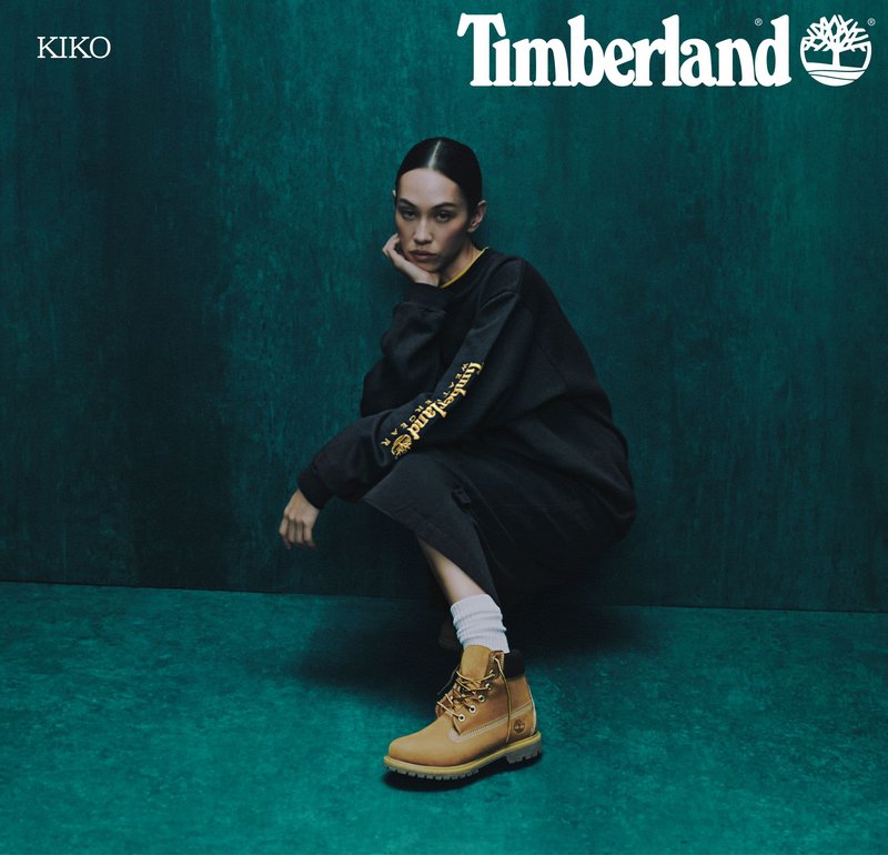 Boczniaki Timberland w kolorze tan z czarnymi akcentami, z metalowymi oczkami i solidnymi podeszwami, w połączeniu z długą, czarną, oversize'ową bluzą.