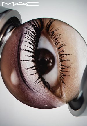 Close-up of an eye with dark lashes, a brown iris, and light skin tones. The circular image features glossy highlights and intricate textures.