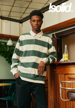 Polo a maniche lunghe a righe in cotone verde e crema, con collo con risvolto e vestibilità comoda, abbinato a pantaloni di denim scuro.