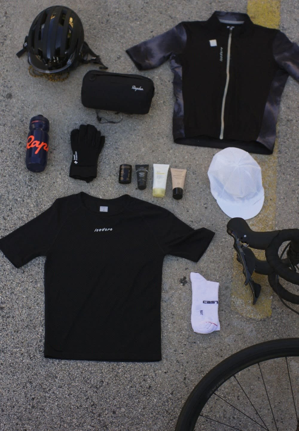 Maillot de cyclisme noir et chemise, gants, casquette blanche, bouteille d'eau, tubes de soins de la peau, sac noir, chaussettes blanches, poignées de vélo, casque noir, asphalte.