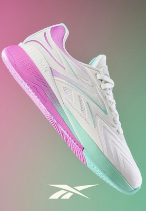 Witte Reebok sneaker met roze zool en turquoise accenten, getoond zwevend tegen een roze en groene verloopachtergrond met daaronder het Reebok-logo.